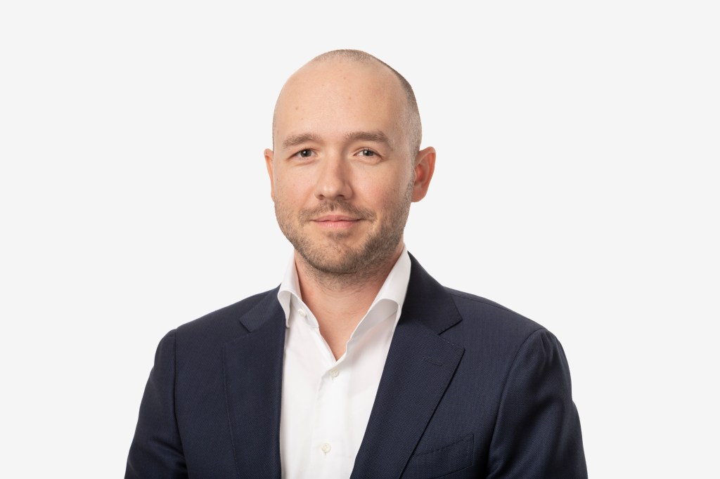 A man in a dark suit and a white shirt against a white background.